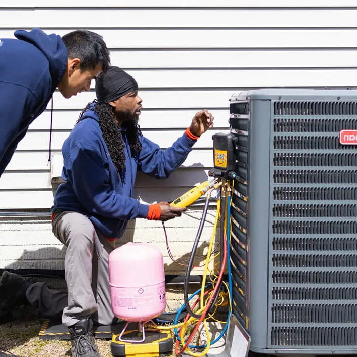 HVAC technicians repairing outdoor AC unit with refrigerant tank and manifold gauges professional air conditioner service